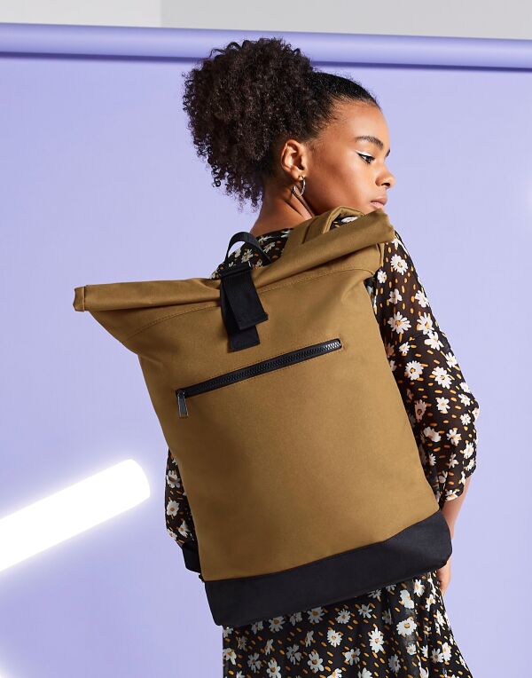 A person wearing the graphite grey Bagbase Roll-Top Backpack, demonstrating its size and comfortable fit.