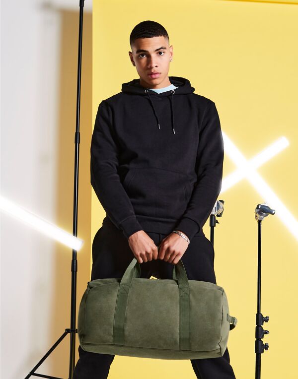 Angled view of the military green Bagbase Vintage Canvas Barrel Bag, showing its cylindrical shape.