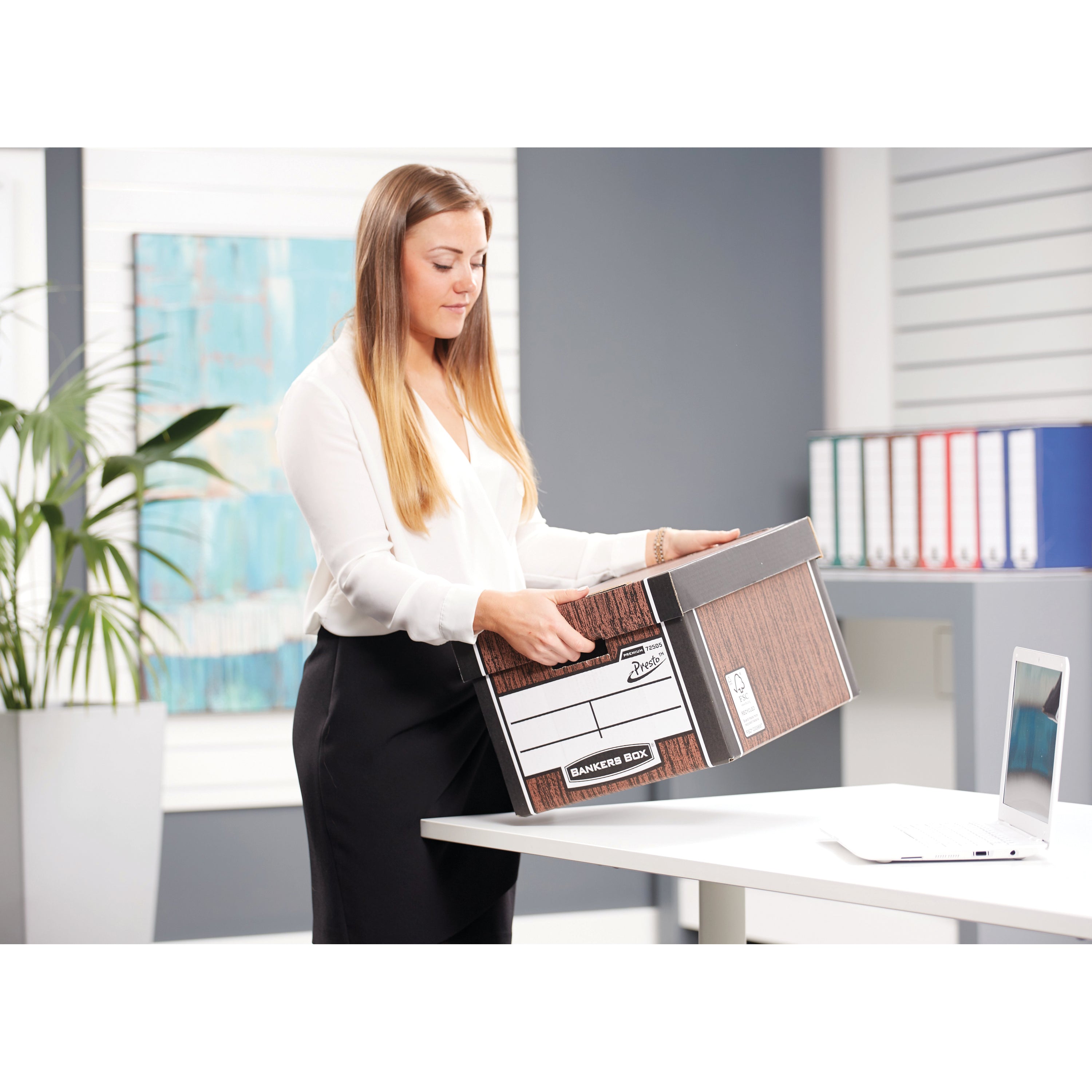 A person placing the lid on the wood grain Bankers Box Premium Classic for secure storage.