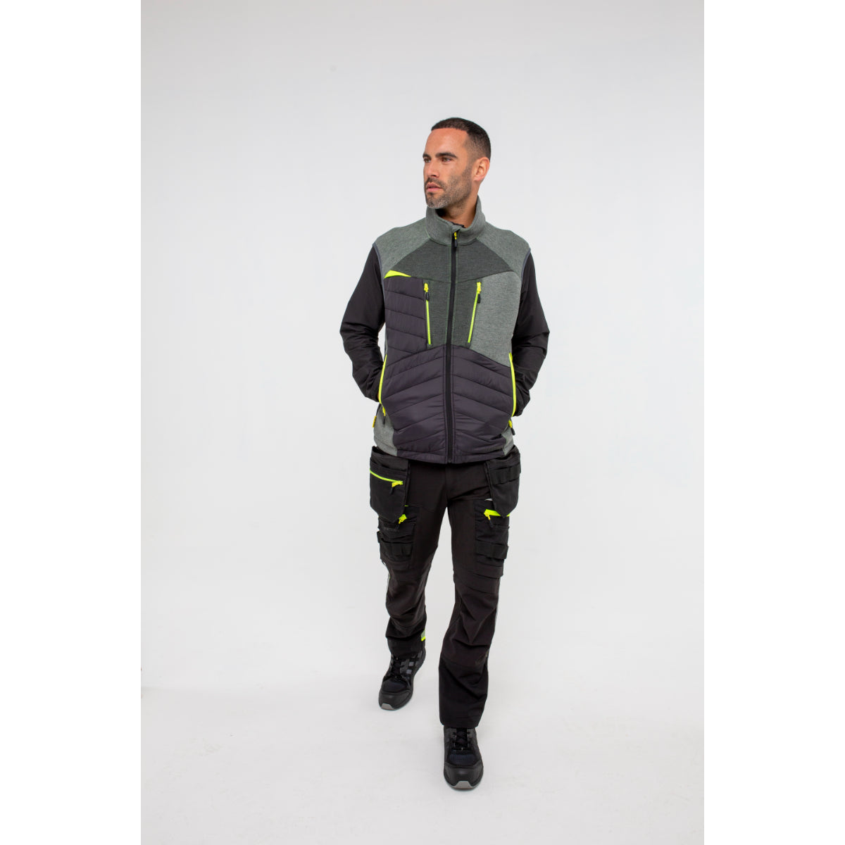 Man in Portwest DX4 Zip Base Layer gilet and work trousers in an industrial setting.