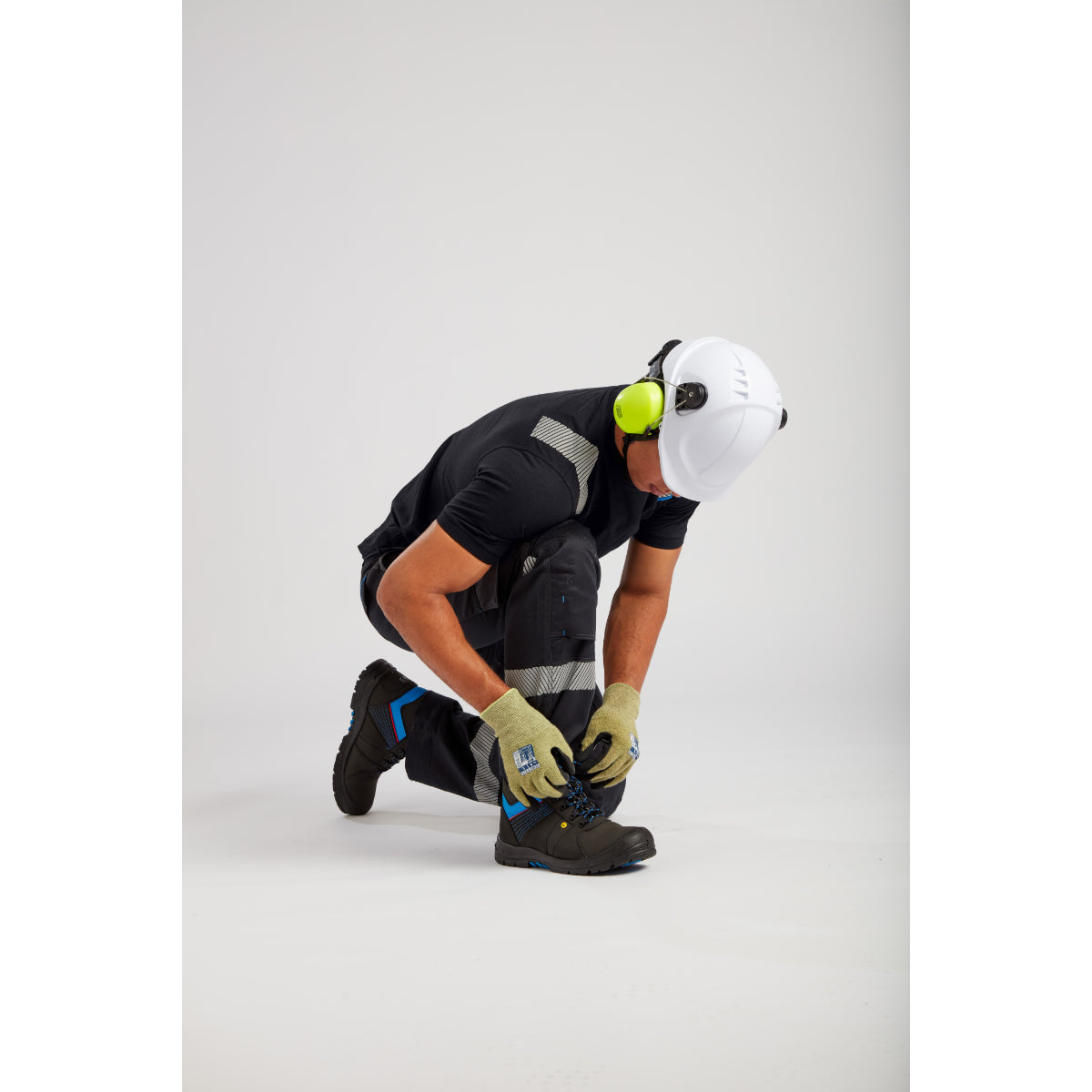 Construction worker tying black safety boots, wearing protective helmet, ear protection and reflective clothing
