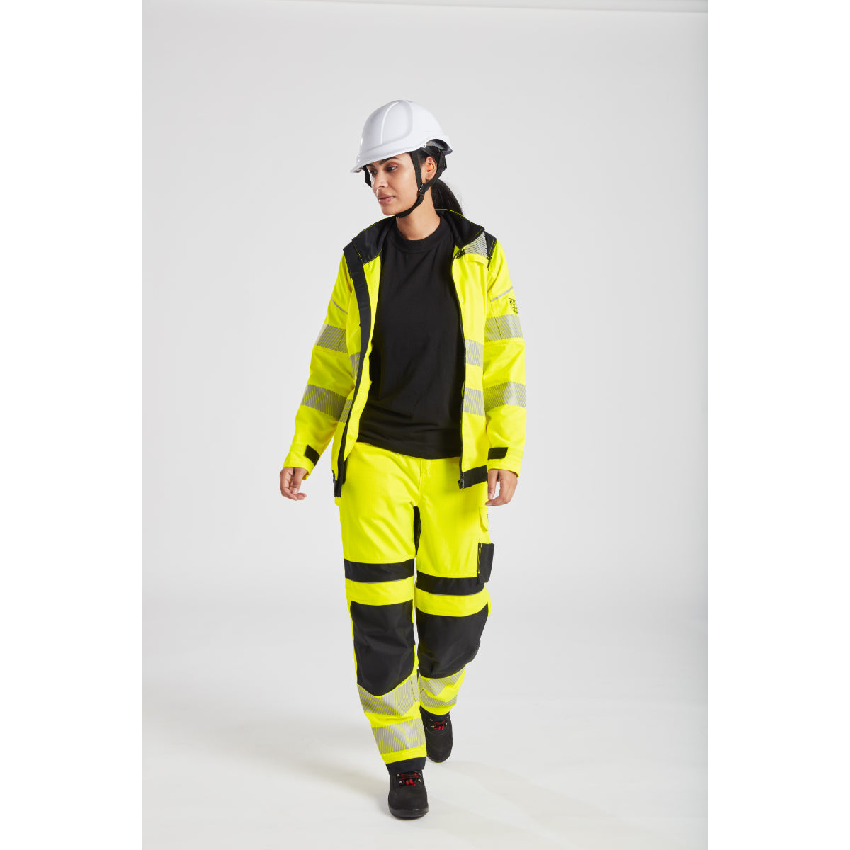 Woman in high-visibility yellow safety gear with reflective stripes, white helmet and black work shoes