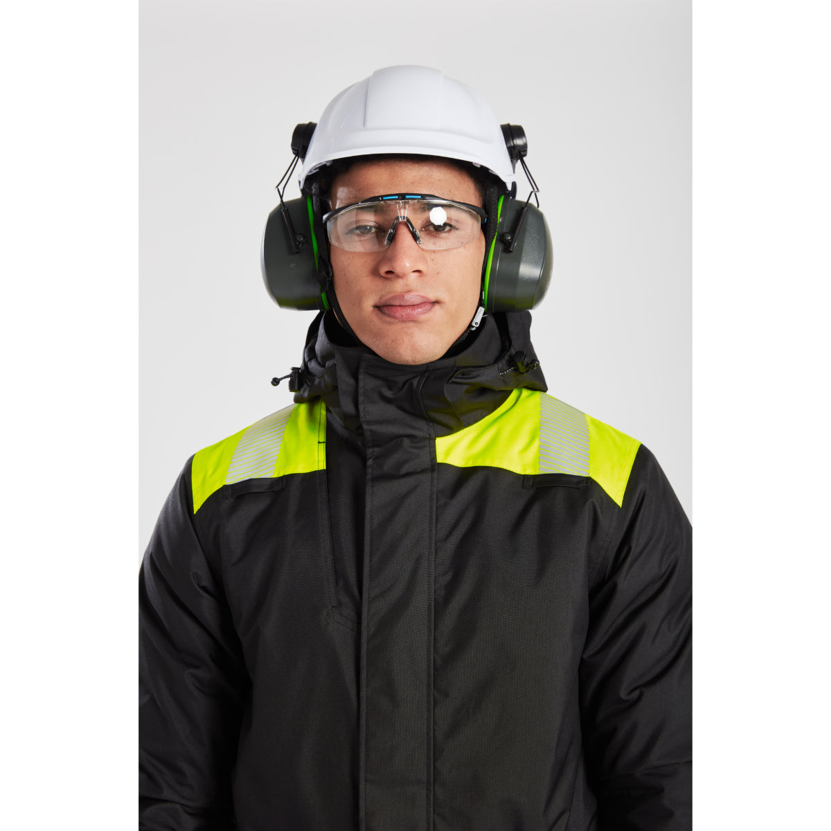 A model wearing the Portwest PW3 coverall with a safety helmet and ear defenders.