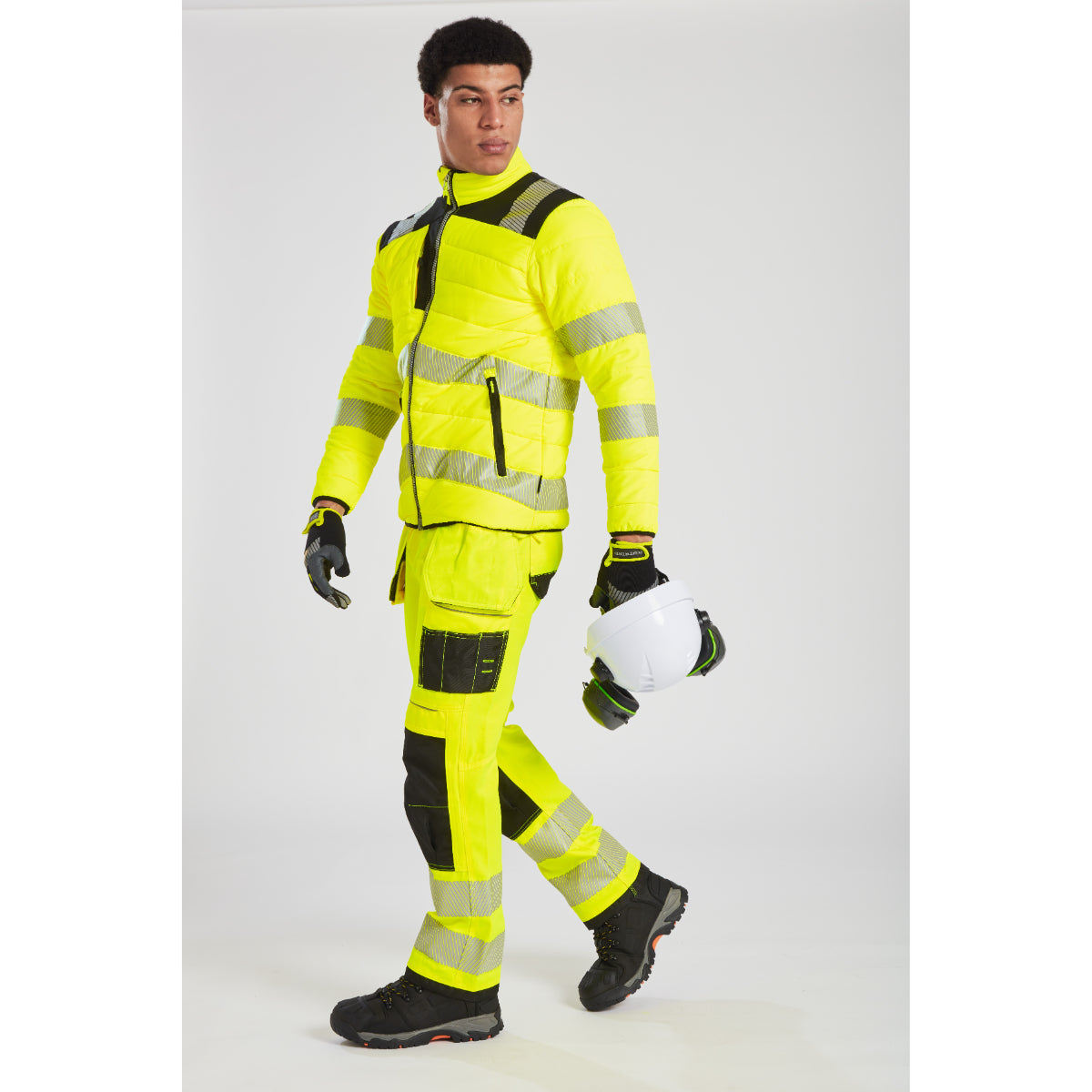 Model in yellow Portwest PW3 Baffle Jacket with safety helmet and glasses.