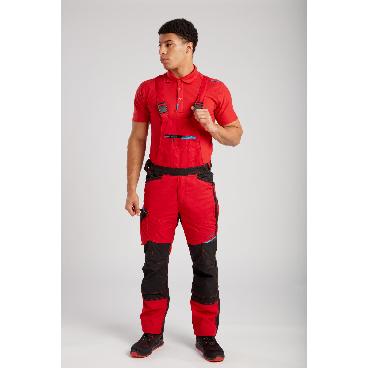 A worker in a dynamic pose wearing the Portwest WX3 Bib and Brace (T704) with safety boots.