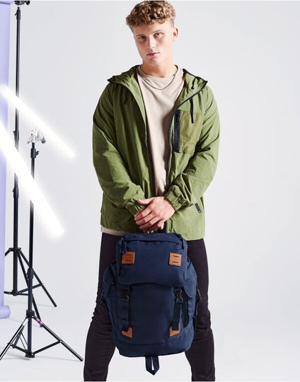 Angled view of the navy and tan Bagbase Urban Explorer Backpack, highlighting its heritage styling.