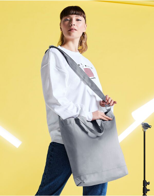 Angled view of the navy Bagbase Canvas Day Bag, showcasing its zippered main compartment and front pocket.