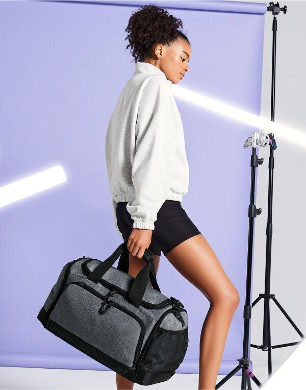 Angled three-quarter view of the heather grey Bagbase Athleisure Holdall, showcasing its modern, sporty design.