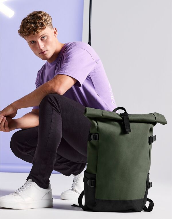 Angled view of the navy and blue Bagbase Block Roll-Top Backpack, showcasing its front zippered pocket.