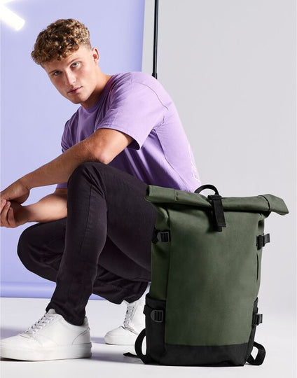 Angled view of the navy and blue Bagbase Block Roll-Top Backpack, showcasing its front zippered pocket.