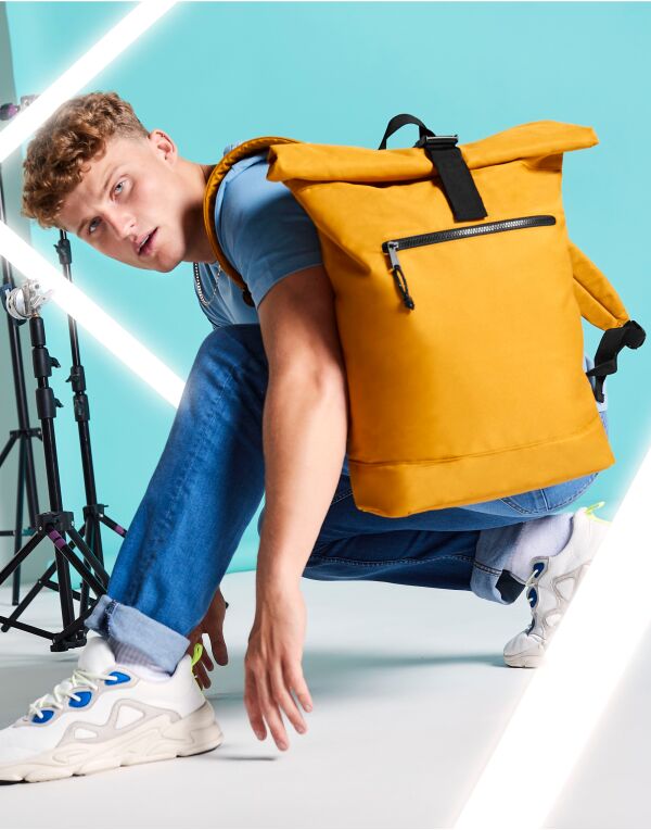 Angled perspective of the Bagbase recycled roll-top backpack, showing the side and front zippered pocket.