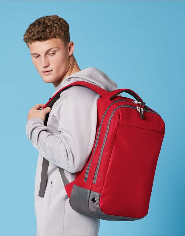 Angled view of the heather grey Bagbase Athleisure Sports Backpack, showing its multiple zippered compartments.