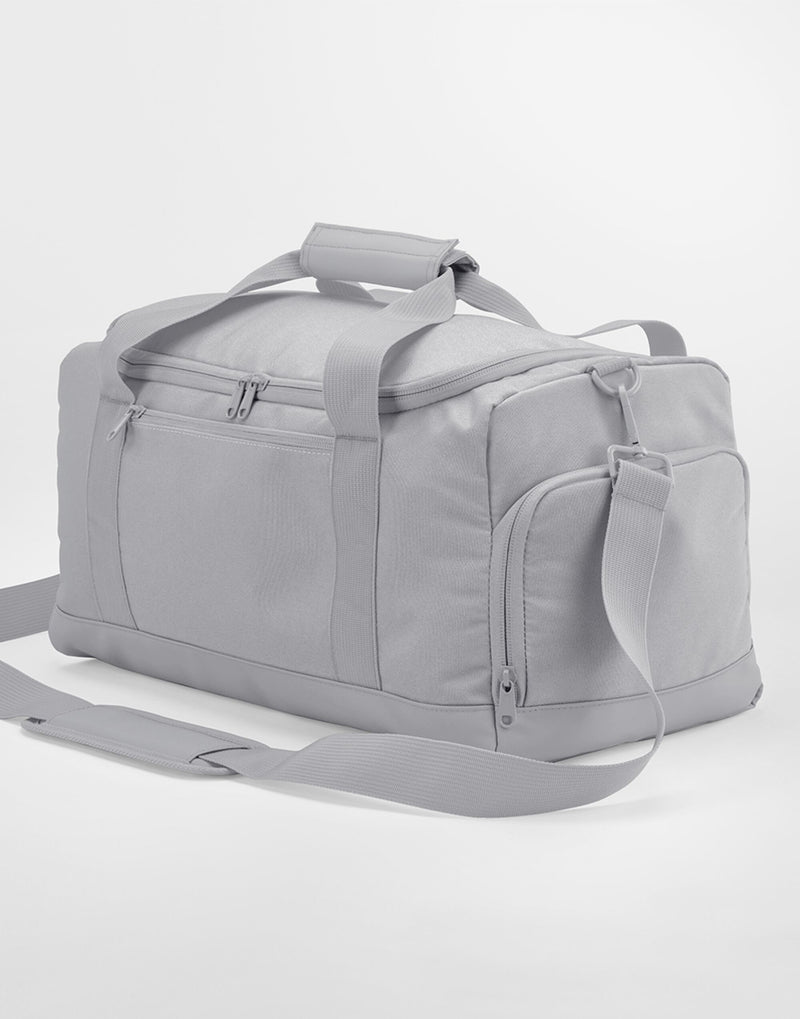 A person carrying the classic red Bagbase Small Training Holdall to show its compact and portable size.
