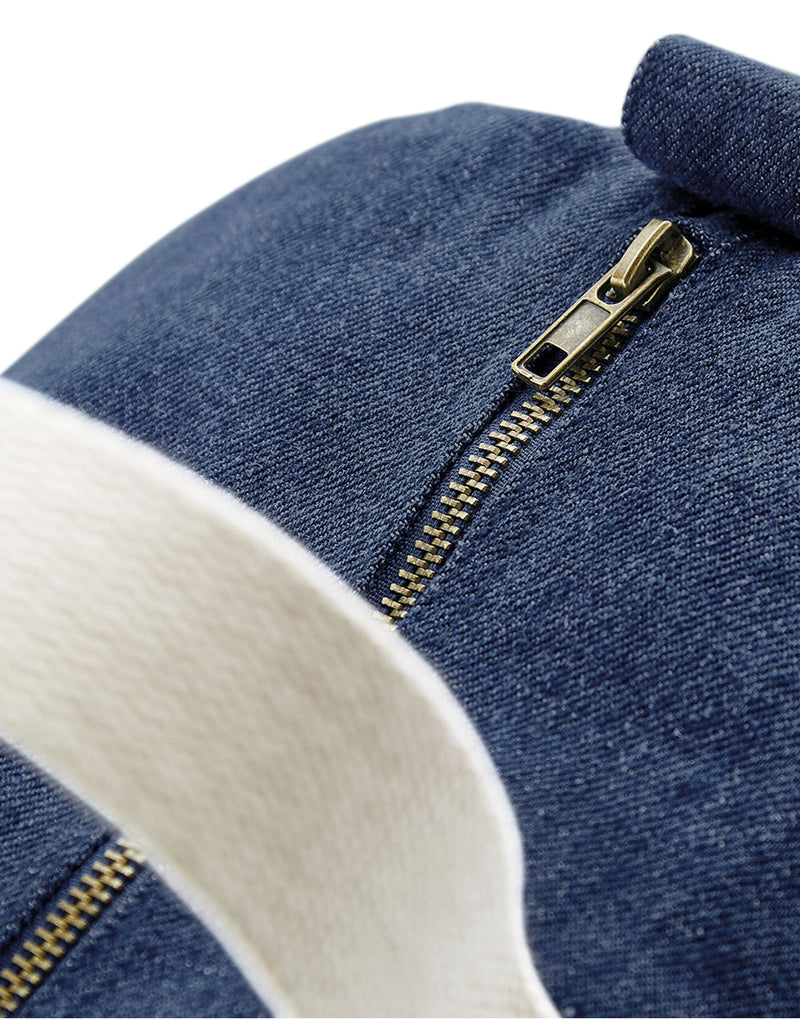 Side profile of the blue denim Bagbase Barrel Bag, showing the end of its main zippered compartment.